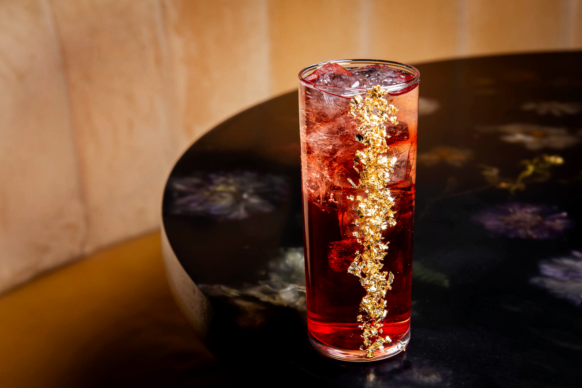 Close up shot of a red cocktail service in a tall glass garnished with gold flakes